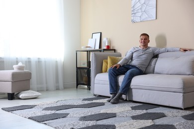 Photo of Happy young man resting on sofa at home, space for text