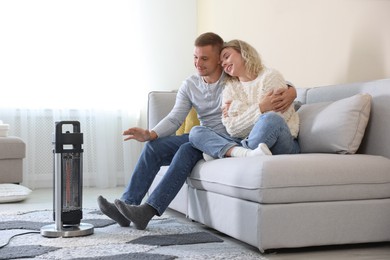 Photo of Happy couple near electric heater on floor at home