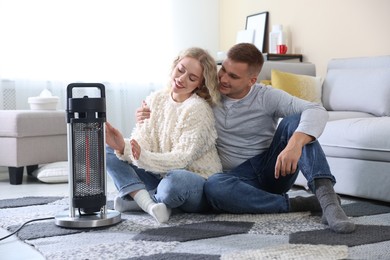 Photo of Happy couple near electric heater on floor at home