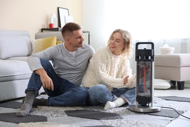 Photo of Happy couple near electric heater on floor at home