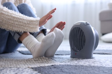 Photo of Young woman near electric heater at home, closeup