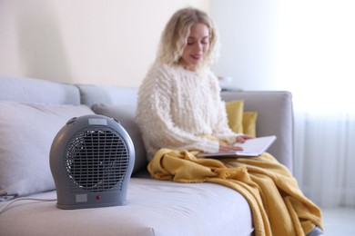 Photo of Young woman reading book near electric heater at home, selective focus