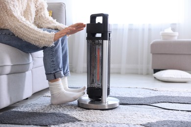 Photo of Young woman near electric heater at home, closeup