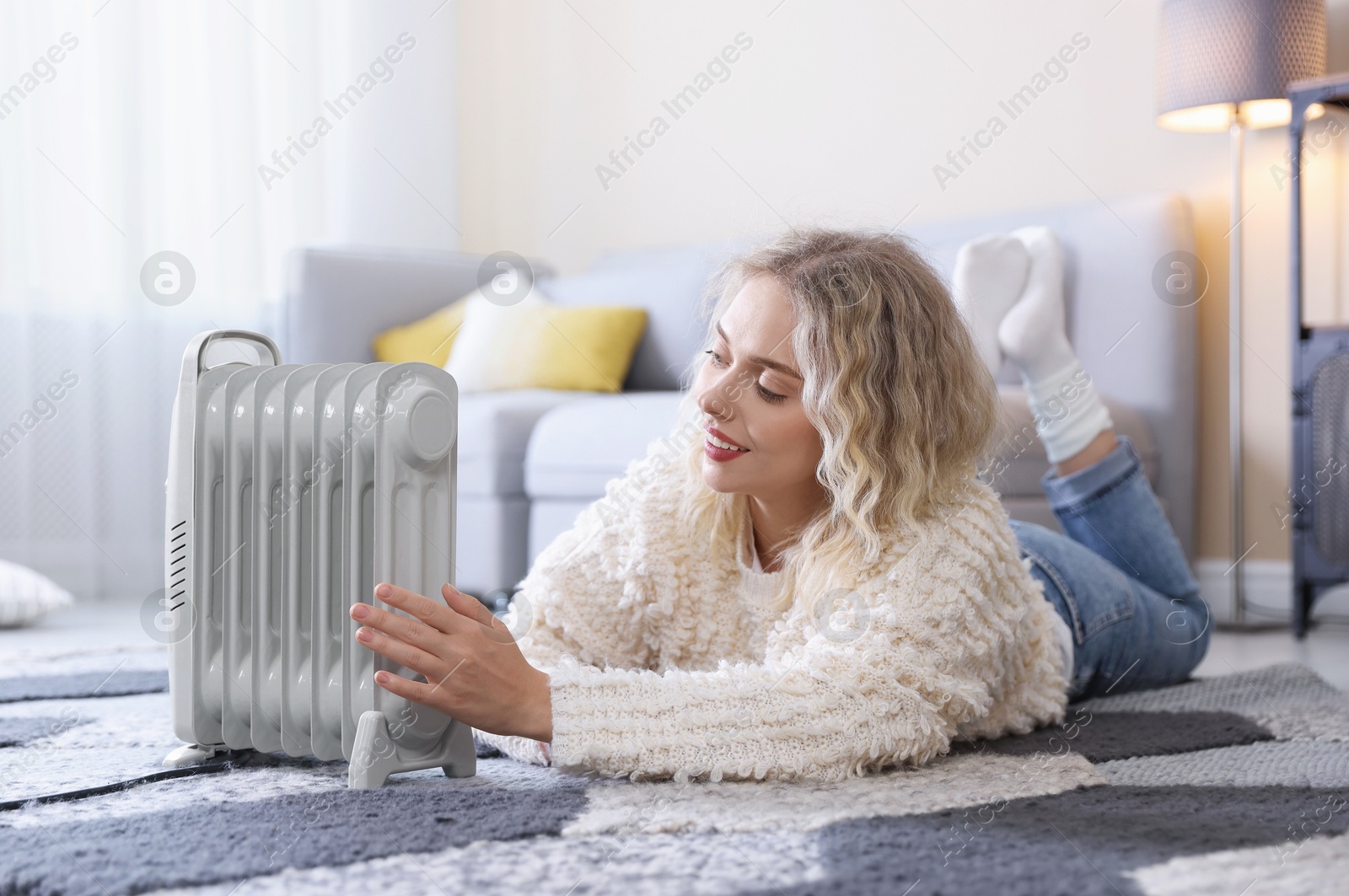Photo of Young woman near electric heater on floor at home