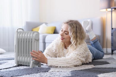 Photo of Young woman near electric heater on floor at home