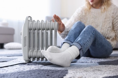 Photo of Young woman near electric heater on floor at home, closeup