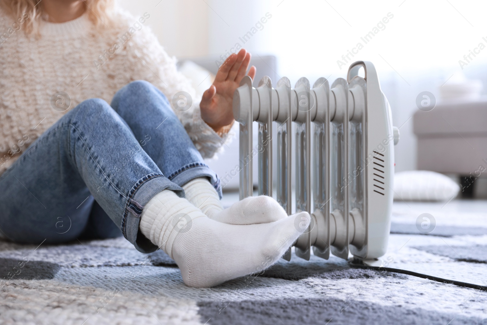 Photo of Young woman near electric heater on floor at home, closeup