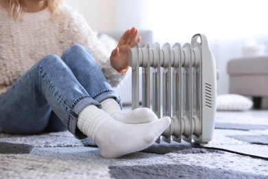 Photo of Young woman near electric heater on floor at home, closeup