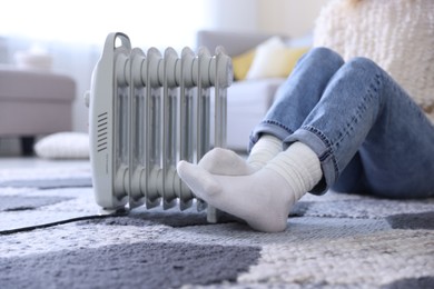 Photo of Young woman near electric heater on floor at home, closeup