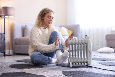 Photo of Young woman near electric heater on floor at home