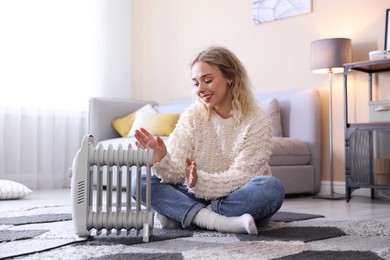Photo of Young woman near electric heater on floor at home