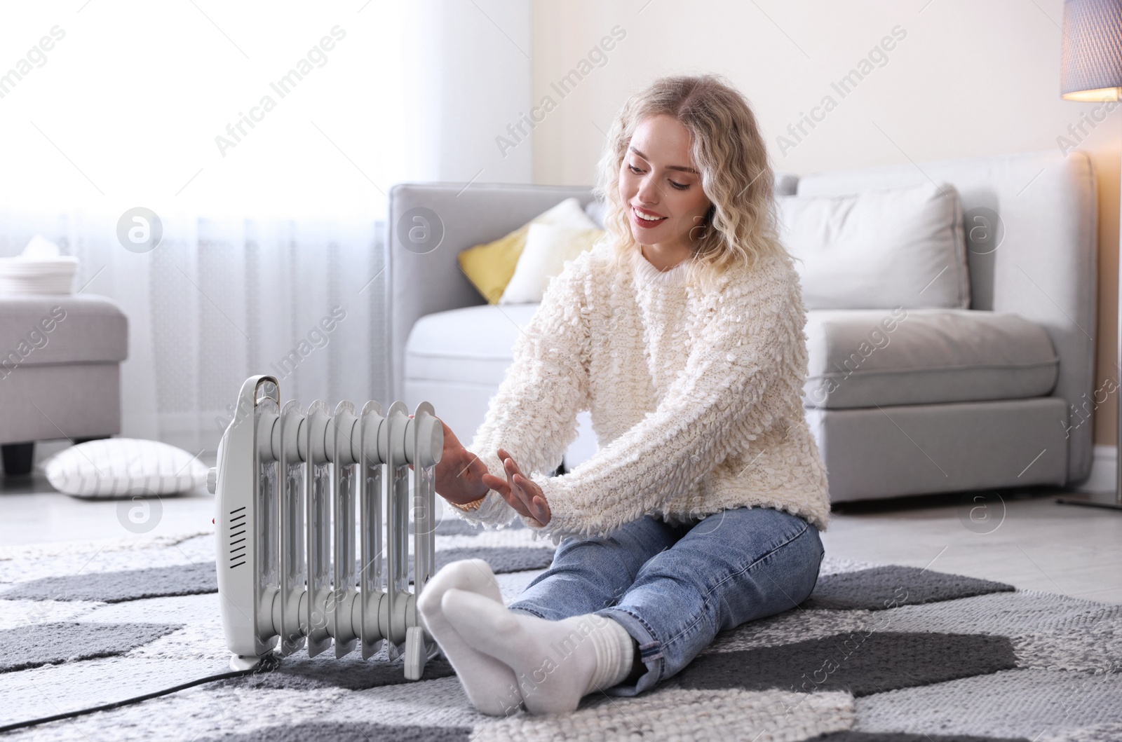 Photo of Young woman near electric heater on floor at home
