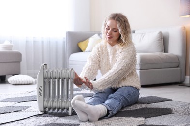 Photo of Young woman near electric heater on floor at home