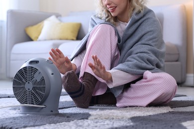 Photo of Young woman near electric heater on floor at home, closeup