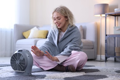 Photo of Young woman near electric heater on floor at home