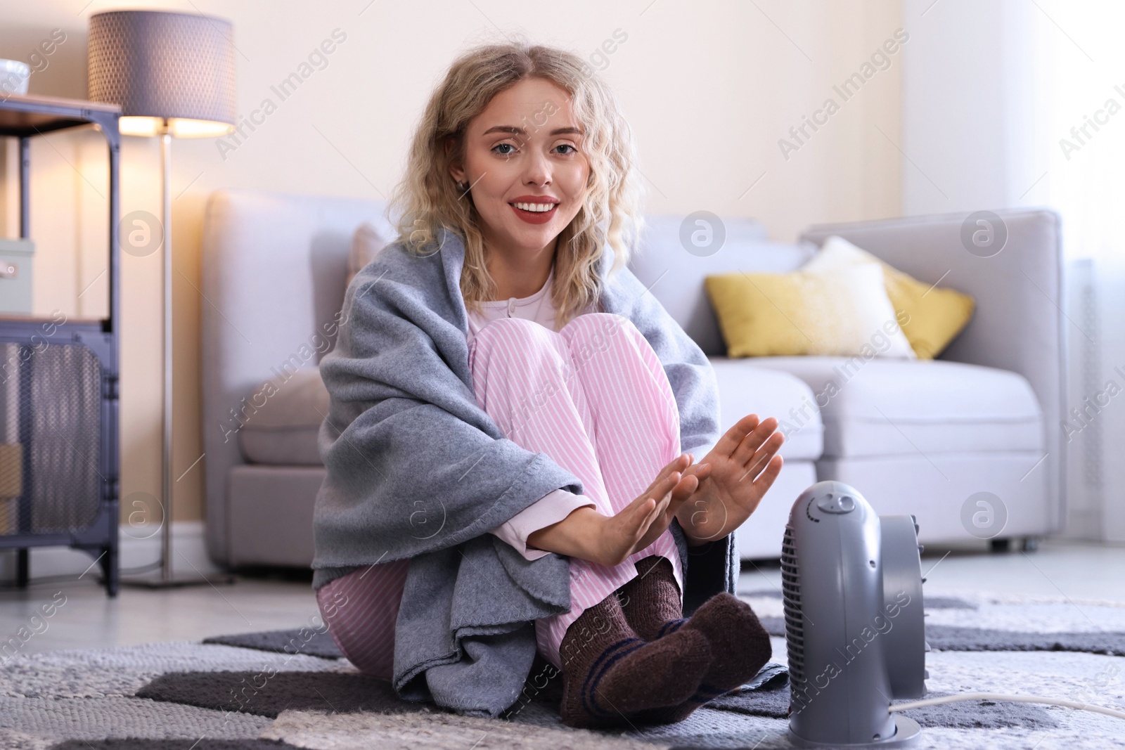 Photo of Young woman near electric heater on floor at home