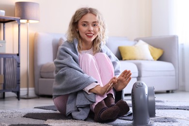 Photo of Young woman near electric heater on floor at home