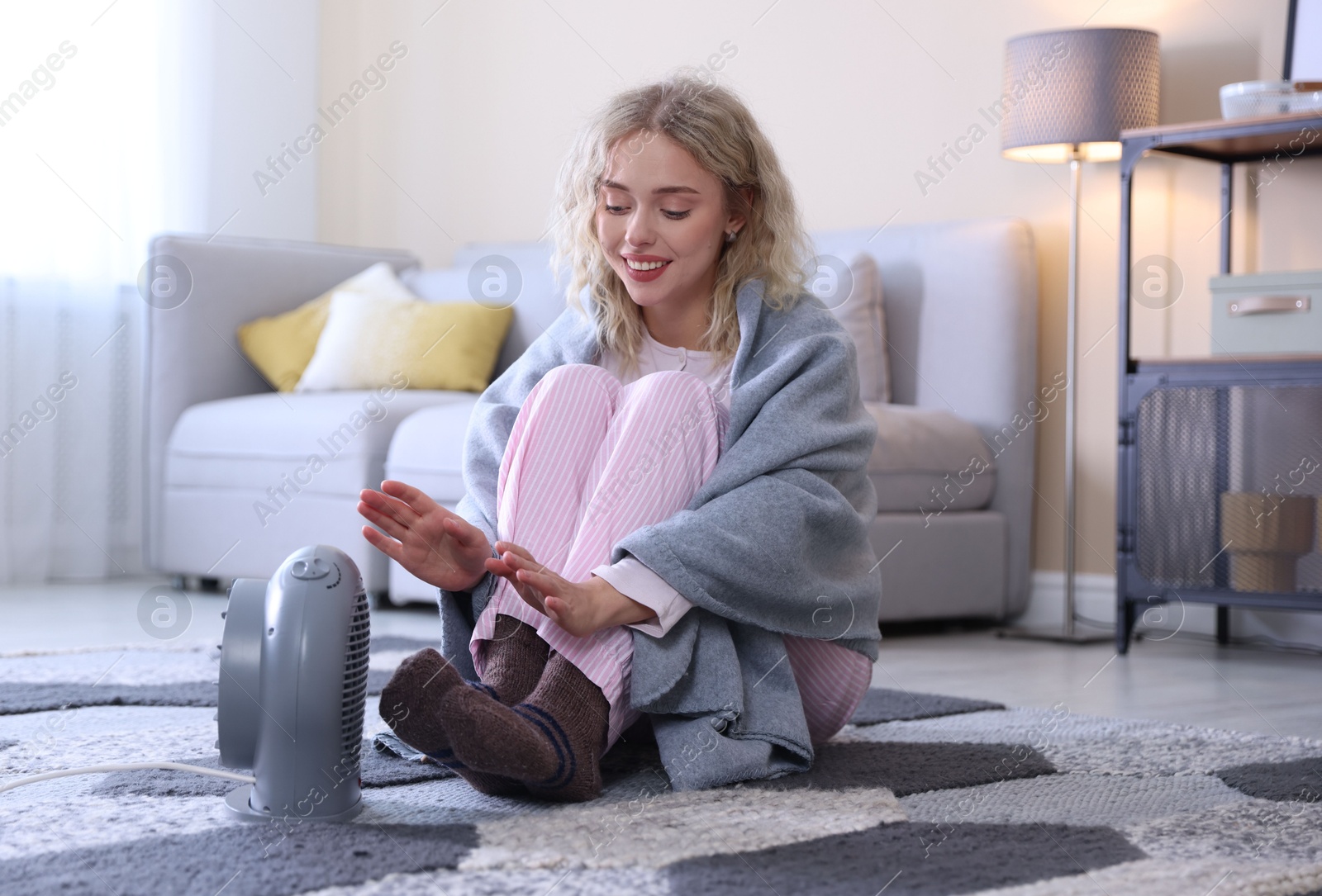 Photo of Young woman near electric heater on floor at home