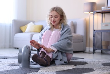 Photo of Young woman near electric heater on floor at home