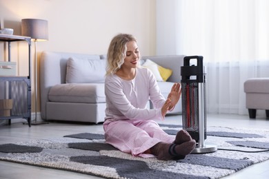 Photo of Young woman near electric heater on floor at home