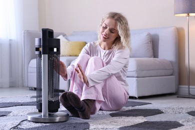 Photo of Young woman near electric heater on floor at home