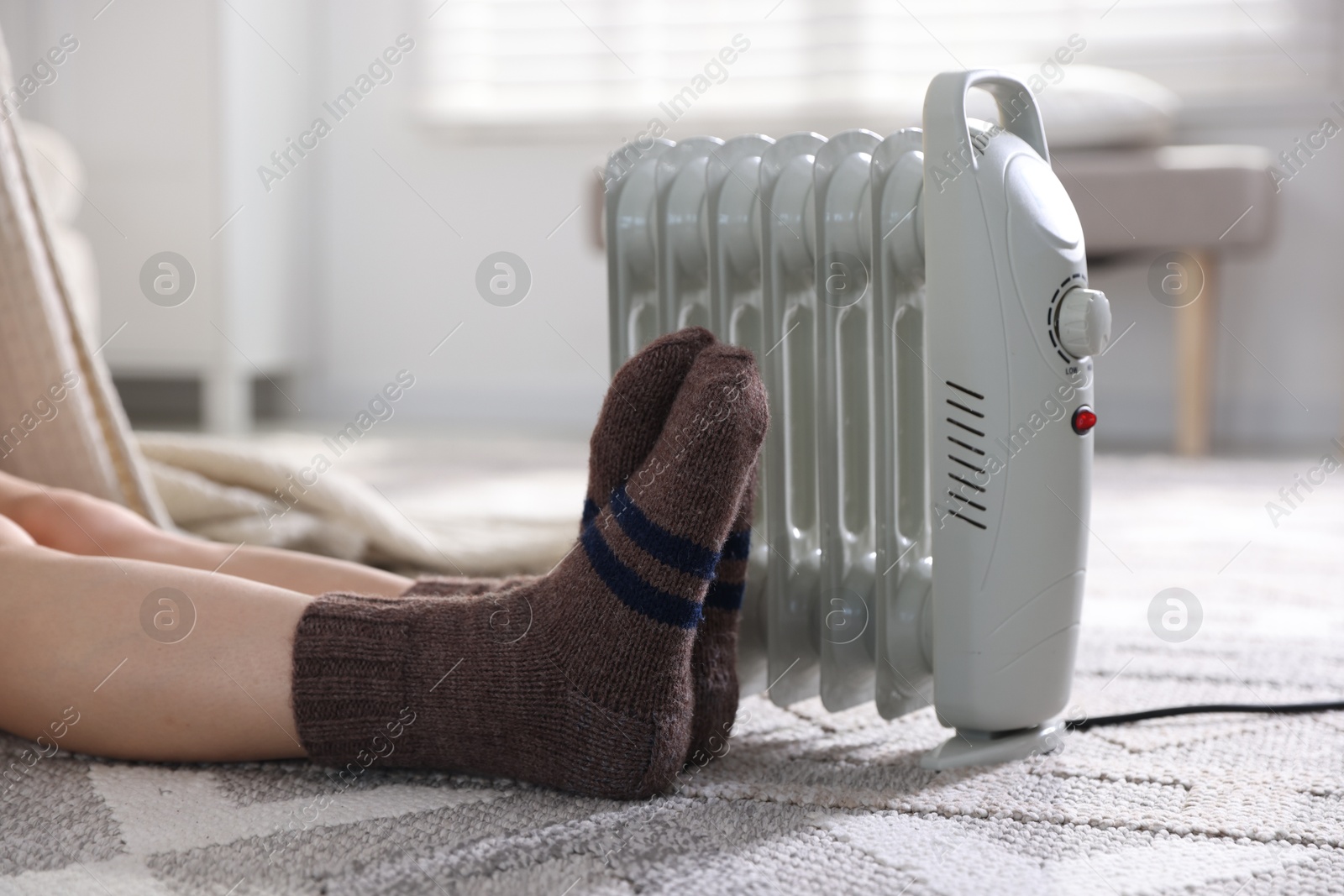 Photo of Young woman near electric heater on floor at home, closeup