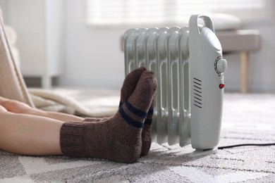 Photo of Young woman near electric heater on floor at home, closeup