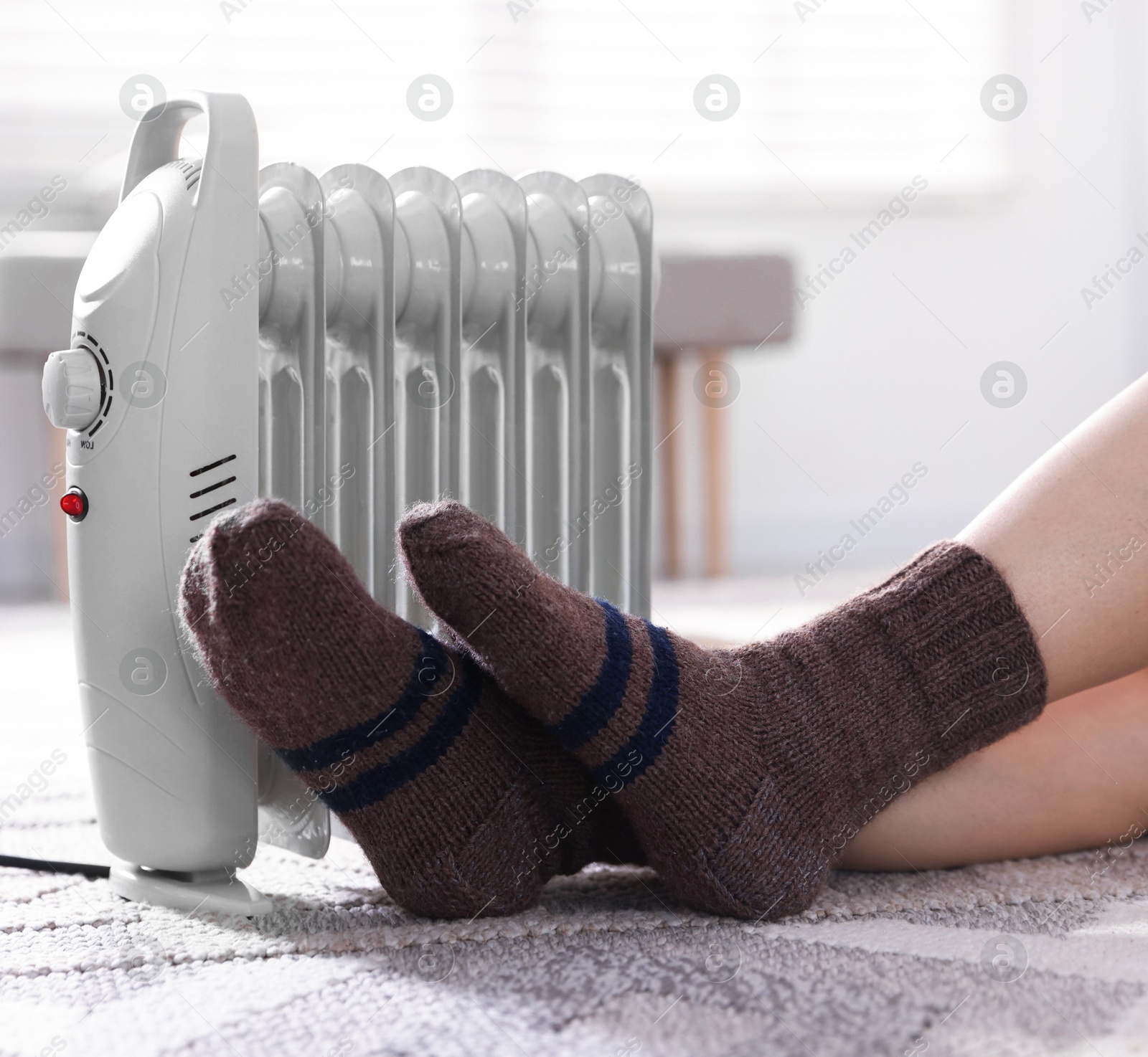 Photo of Young woman near electric heater on floor at home, closeup