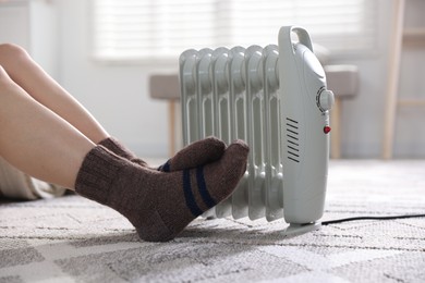 Photo of Young woman near electric heater on floor at home, closeup