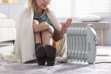 Photo of Young woman near electric heater on floor at home, closeup