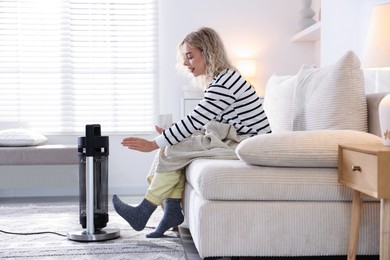Photo of Young woman near electric heater on floor at home