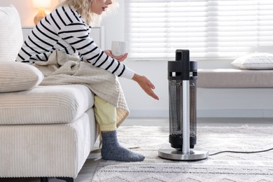 Photo of Young woman near electric heater on floor at home, closeup