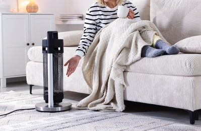 Photo of Young woman near electric heater on floor at home, closeup