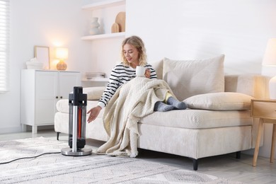 Photo of Young woman near electric heater on floor at home