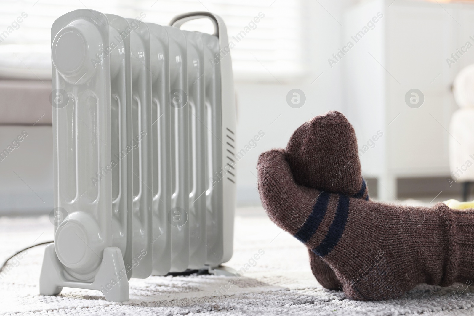 Photo of Young woman near electric heater on floor at home, closeup