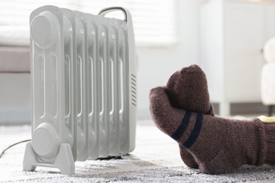 Photo of Young woman near electric heater on floor at home, closeup