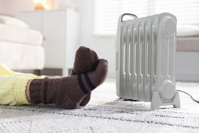 Photo of Young woman near electric heater on floor at home, closeup
