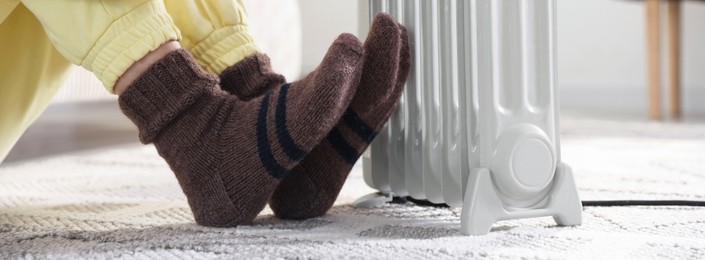 Photo of Young woman near electric heater on floor at home, closeup