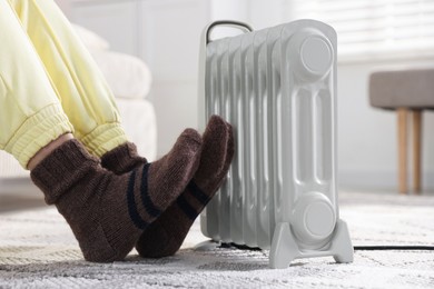 Photo of Young woman near electric heater on floor at home, closeup