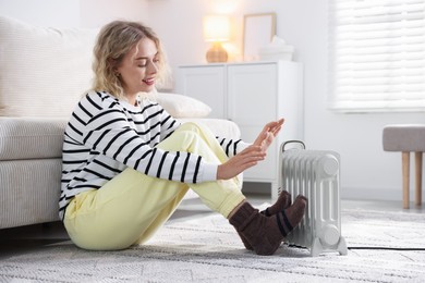 Photo of Young woman near electric heater on floor at home