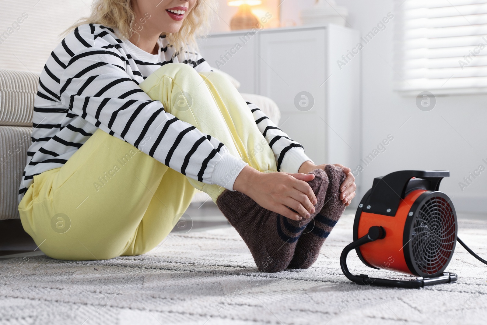 Photo of Young woman near electric heater on floor at home, closeup