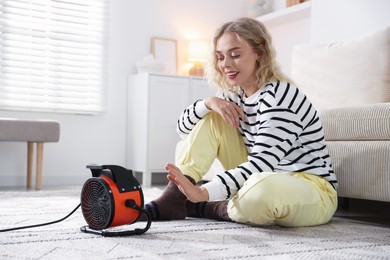 Photo of Young woman near electric heater on floor at home