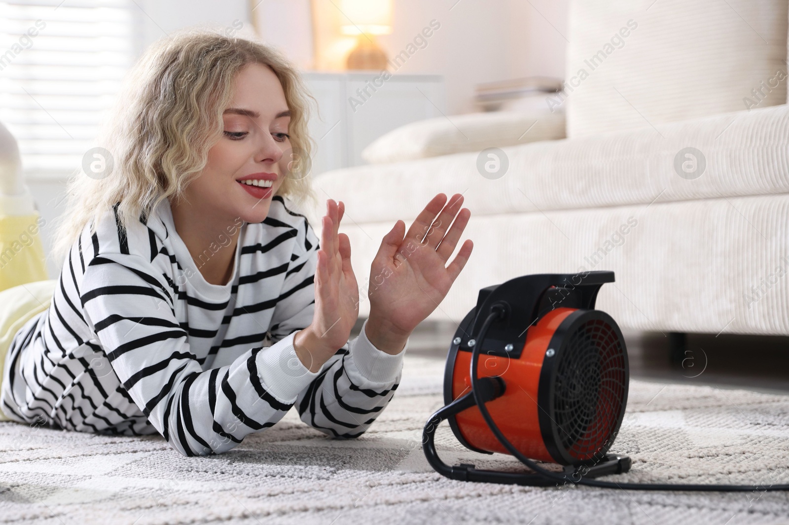 Photo of Young woman near electric heater on floor at home