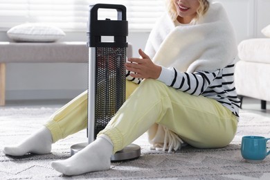 Photo of Young woman with cup of drink near electric heater at home, closeup