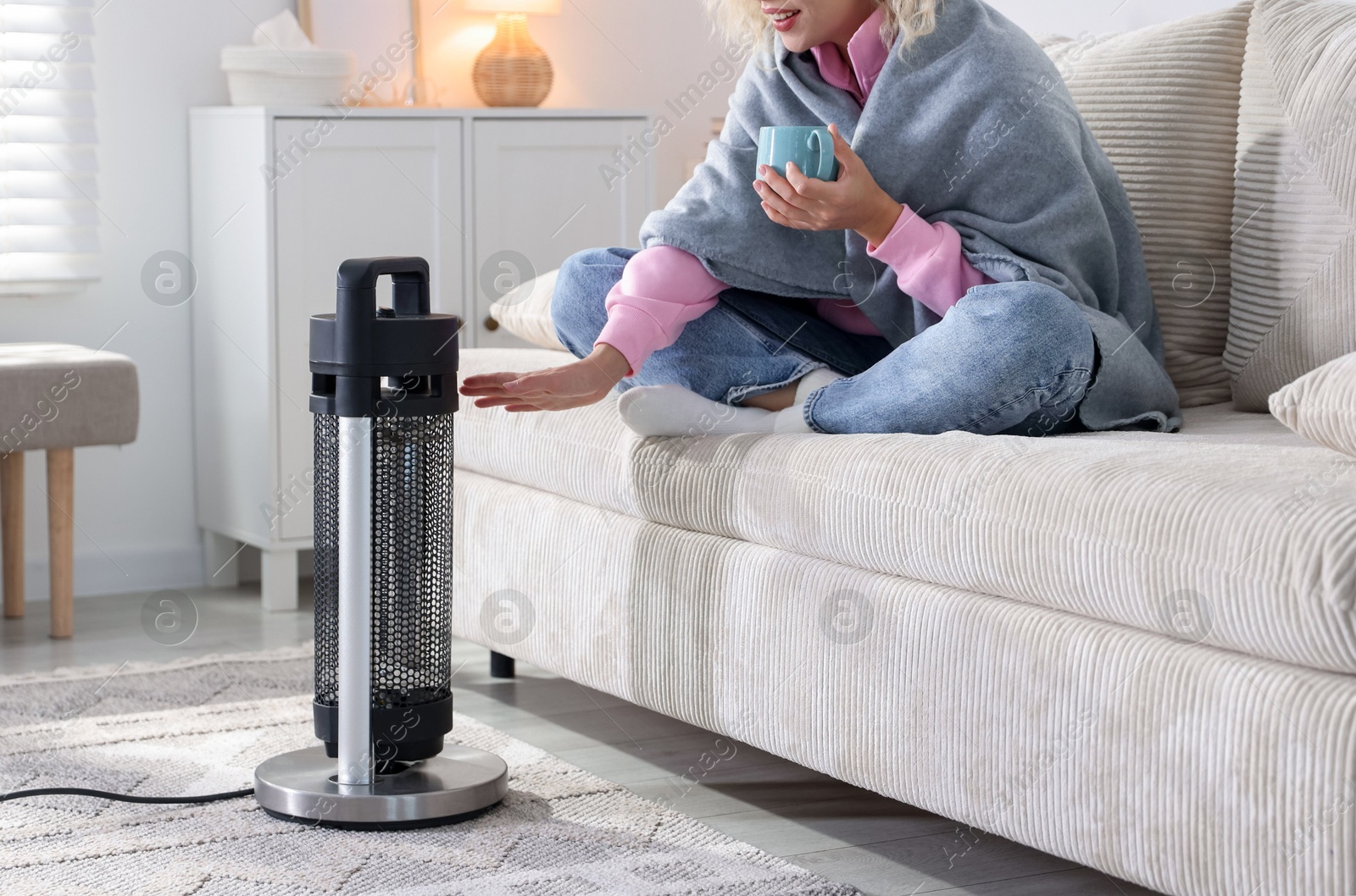 Photo of Young woman with cup of drink near electric heater at home, closeup