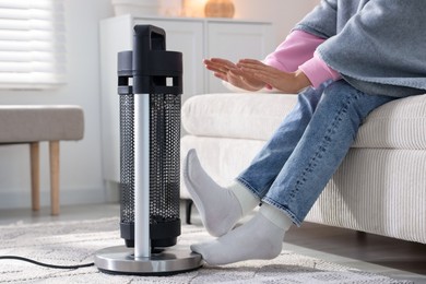 Photo of Young woman near electric heater at home, closeup
