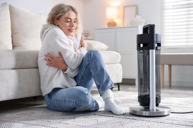 Photo of Young woman near electric heater on floor at home