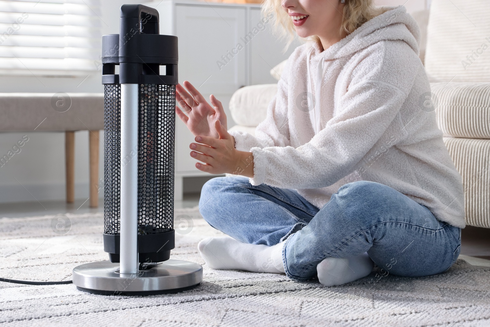 Photo of Young woman near electric heater on floor at home, closeup