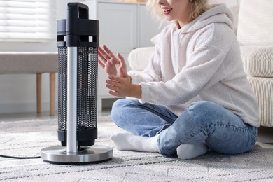 Photo of Young woman near electric heater on floor at home, closeup