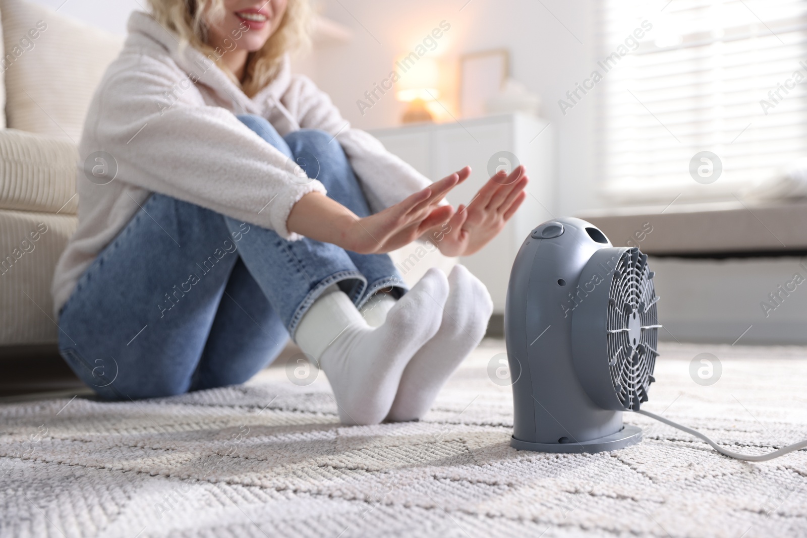 Photo of Young woman near electric heater on floor at home, closeup